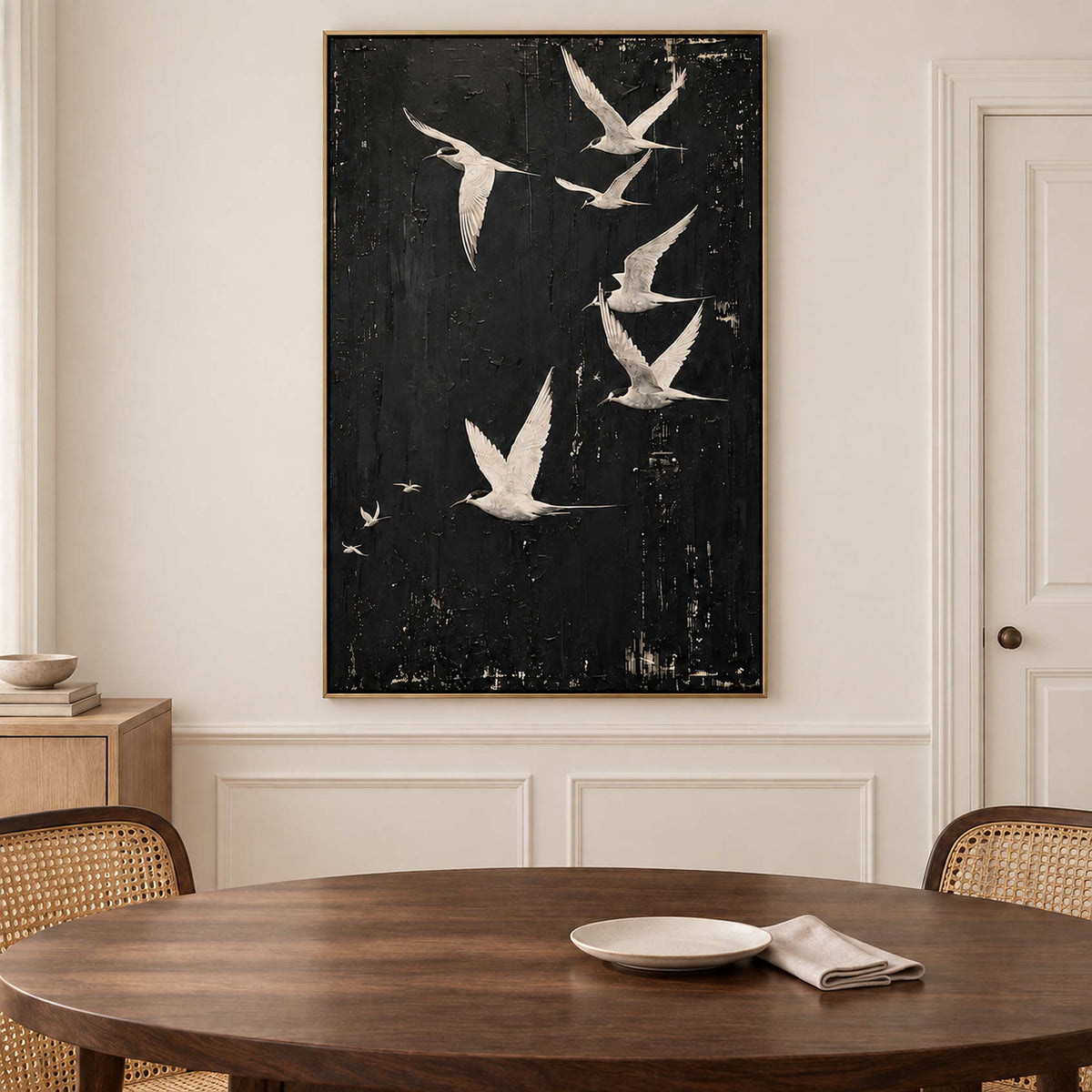 White birds flying across a charcoal-black sky in a gold frame, displayed above a dining table.