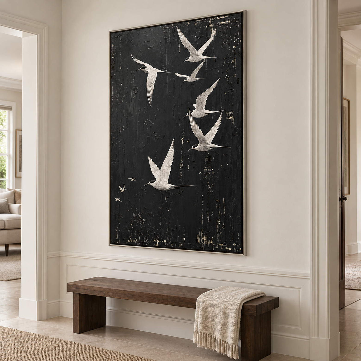 White birds flying across a charcoal-black sky in a silver frame, displayed in a hallway.