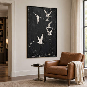 White birds flying across a charcoal-black sky in a black frame, displayed beside seating in a lounge.
