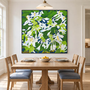 Artwork showing white flowers and broad green leaves over a deep blue ground in a dining area beside the table, with a black frame.