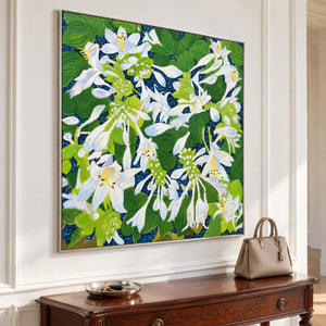 White flowers and broad green leaves over a deep blue ground in an artwork with a silver-colored frame, displayed in an entryway above a console or bench.