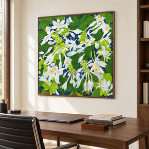Artwork showing white flowers and broad green leaves over a deep blue ground in a study with a desk, with a brown wood-look frame.