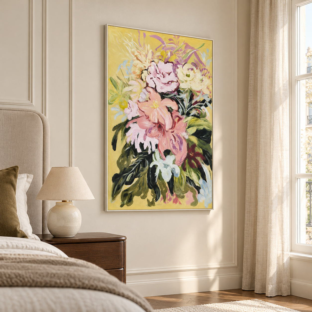 Large pink and cream flowers with dark green leaves on a warm yellow ground in an artwork with a white frame, displayed in a bedroom near the bed.