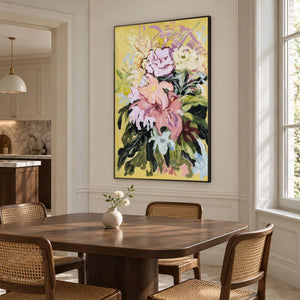 In a dining area beside the table, an artwork with a black frame shows large pink and cream flowers with dark green leaves on a warm yellow ground.