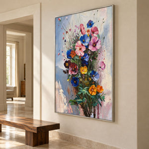 Artwork showing pink, blue and orange flowers on fine stems with dark green leaves against pale blue in a hallway above a bench, with a silver-colored frame.