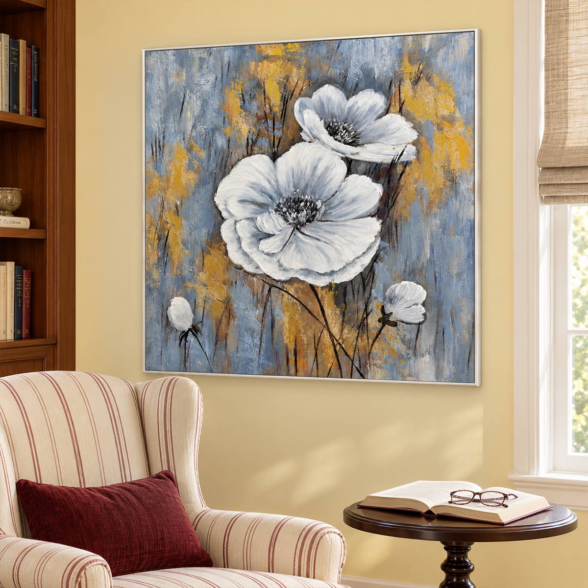 Artwork showing two large white flowers and small buds on a blue-gray ground with ochre marks beside a reading chair, with a white frame.