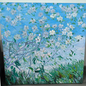 Photographed view of white flowering branches against blue sky above green grass, with the artwork edge and surrounding background visible.