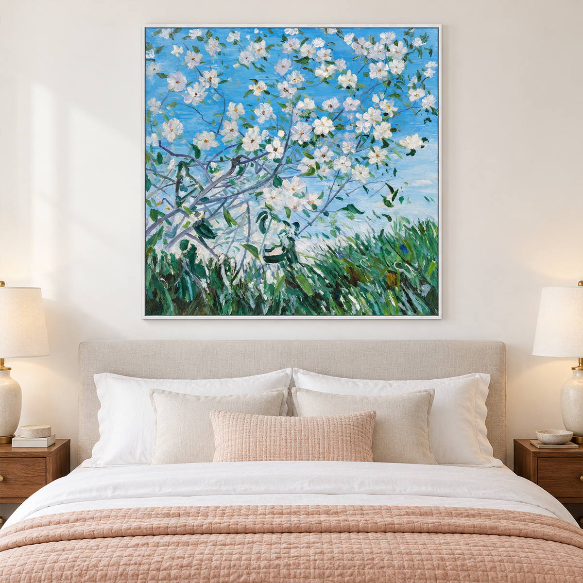 In a bedroom near the bed, an artwork with a white frame shows white flowering branches against blue sky above green grass.