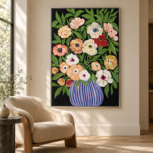 Artwork showing cream, peach and red flowers with green leaves in a purple-blue striped vase on black beside a reading chair, with a silver-colored frame.
