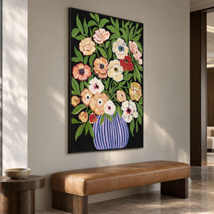 Cream, peach and red flowers with green leaves in a purple-blue striped vase on black in an artwork with a black frame, displayed in a seating area.