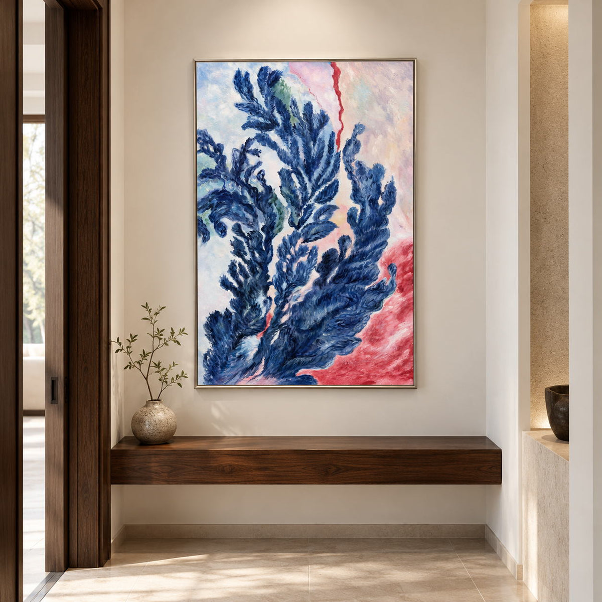 In a hallway above a bench, an artwork with a silver-colored frame shows branching deep blue forms curling upward over pale pink, cream and red.