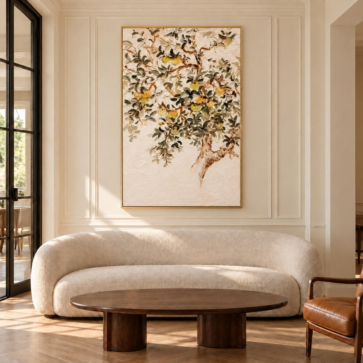 Branching gray-green leaves and pale yellow-green fruit on cream in an artwork with a gold-colored frame, displayed in a living room above seating.