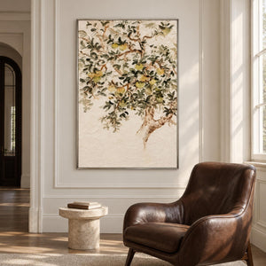 Artwork showing branching gray-green leaves and pale yellow-green fruit on cream beside a reading chair, with a silver-colored frame.