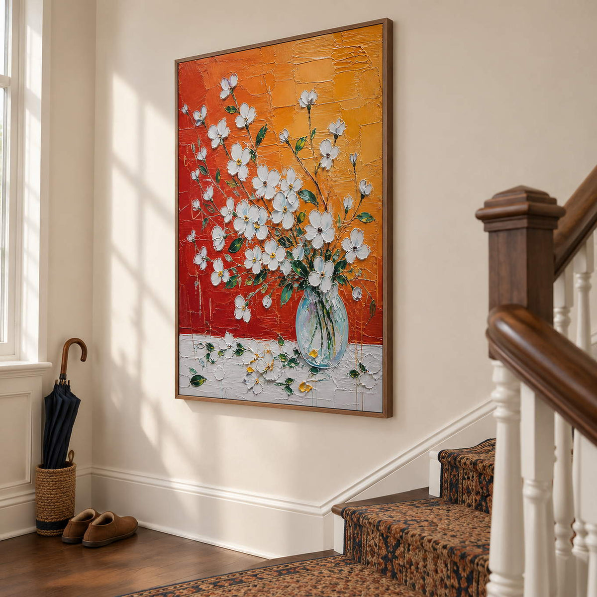 White blossoms in a glass vase against an orange and red background in a brown wood frame on a stair landing.