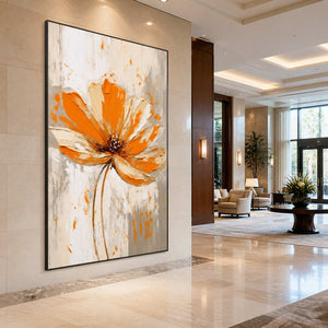 Black framed orange floral painting on a pale hotel lobby wall near cream seating.