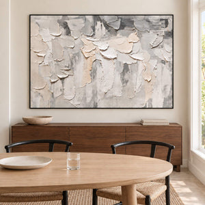 Overlapping ivory and gray raised strokes on a pale ground in a black frame, displayed above a dining table.