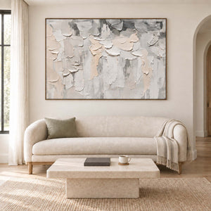 Overlapping ivory and gray raised strokes on a pale ground in a brown wood frame, displayed above a sofa in a living room.