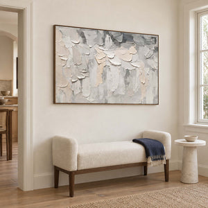 Overlapping ivory and gray raised strokes on a pale ground in a brown wood frame, displayed beside seating in a lounge.