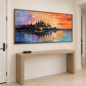 A distant castle reflected in water beneath an orange sunset in a brown wood frame, displayed above an entryway console.