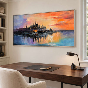 A distant castle reflected in water beneath an orange sunset in a silver frame, displayed in a home office.