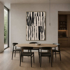 Gold framed black and white artwork beside a wooden dining table and black chairs.