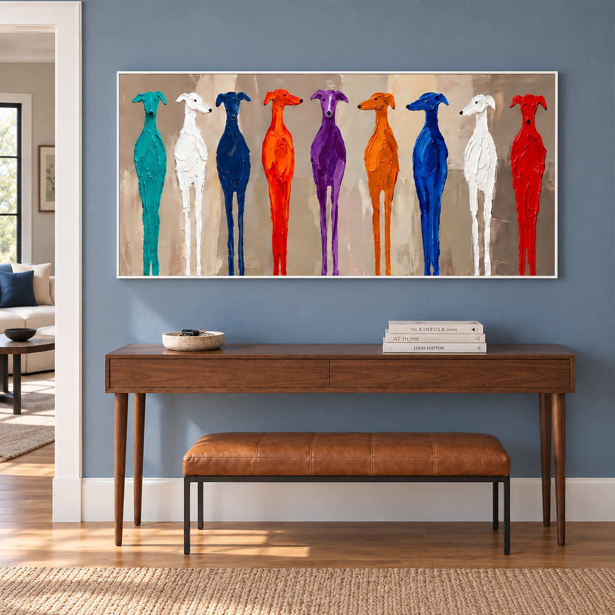Cheerful Company in a white frame above a wood console and tan leather bench against a blue hallway wall.