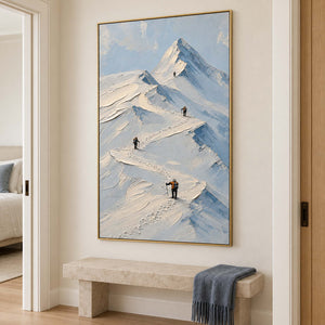 Small climbers following ridges across snowy mountains in a gold frame, displayed in a hallway.