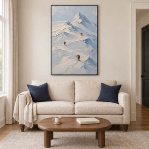 Small climbers following ridges across snowy mountains in a black frame, displayed above a sofa in a living room.