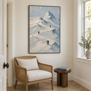 Small climbers following ridges across snowy mountains in a black frame, displayed beside seating in a lounge.