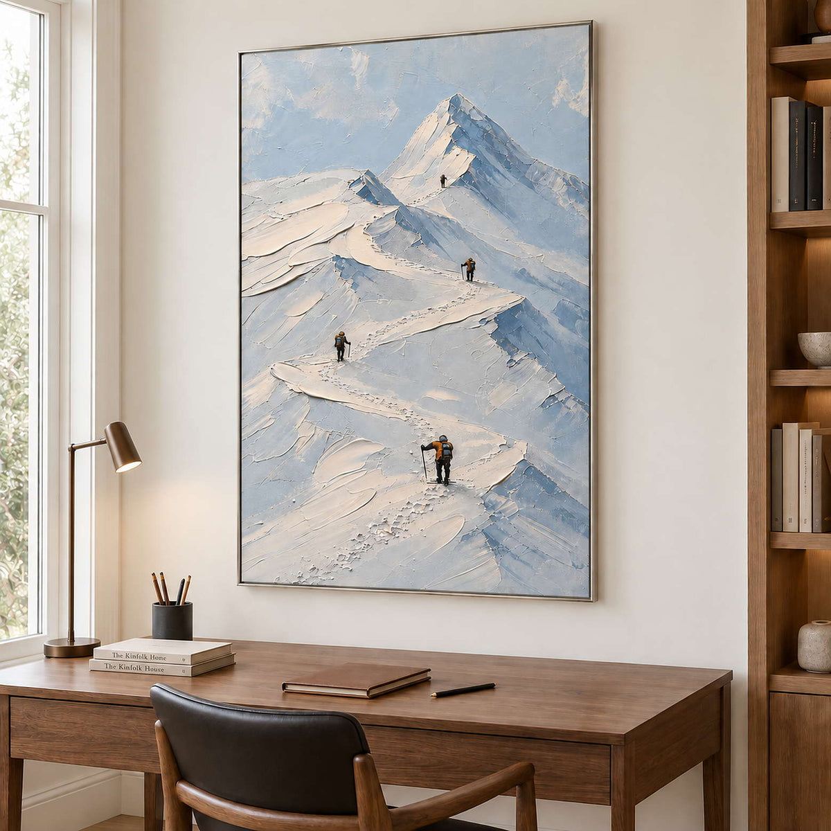 Small climbers following ridges across snowy mountains in a silver frame, displayed in a home office.