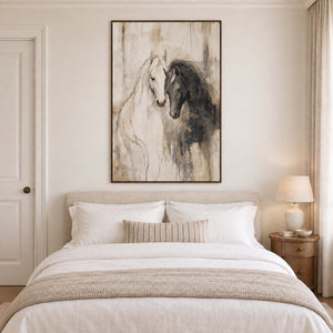 A white horse and a dark horse leaning close on an ivory ground in a brown wood frame, displayed above a bed.