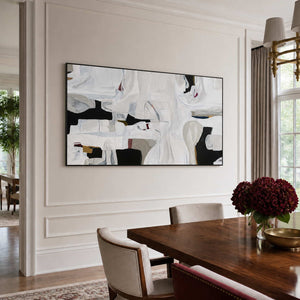Black framed white abstract artwork beside a wooden dining table with burgundy flowers.