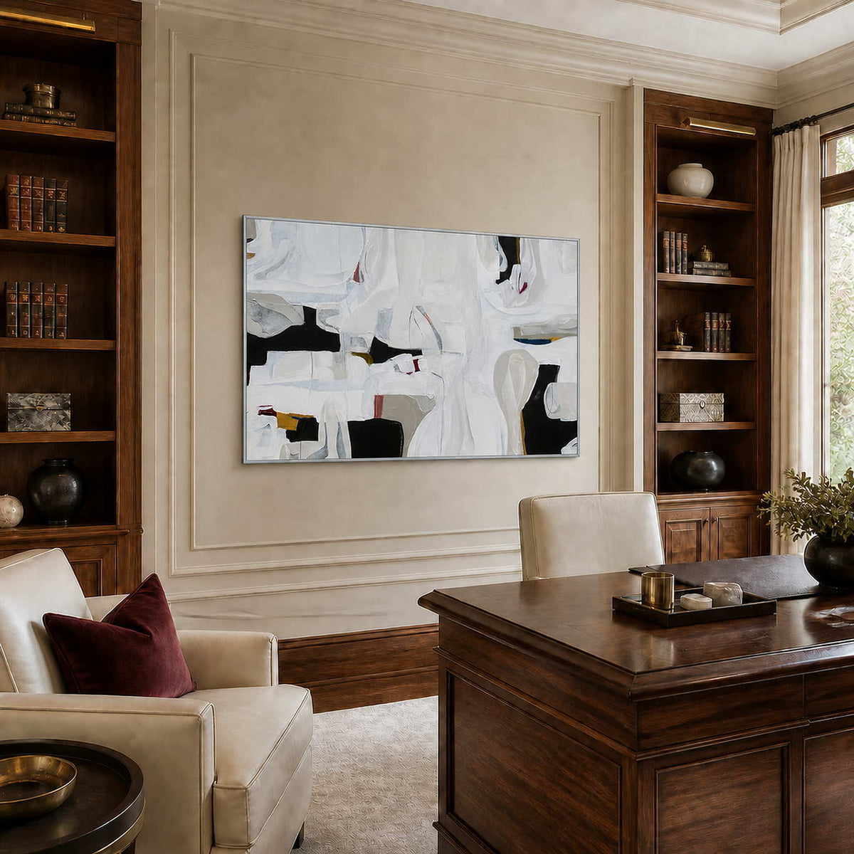 Silver framed white abstract artwork between wooden bookshelves behind a home office desk.