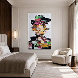 White framed multicolored portrait beside a neutral bed and rounded cream chair in a bedroom.