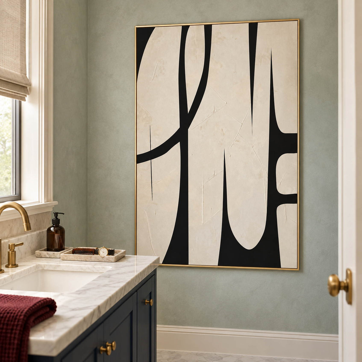 Cream and black abstract painting with elongated forms and a sweeping arc in a gold frame beside a bathroom vanity.
