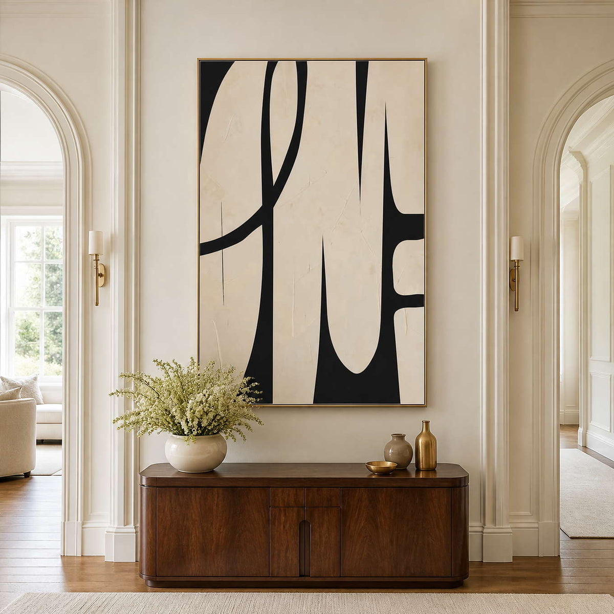 Gold framed cream and black abstract artwork above a rounded wooden console in a hallway.