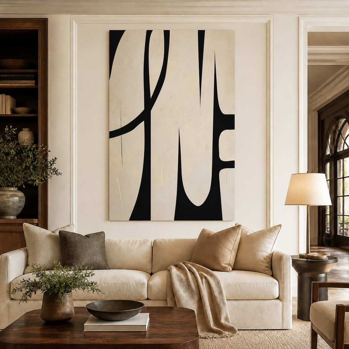 Frameless cream and black curved artwork above a cream sofa beside bookshelves and warm wood.