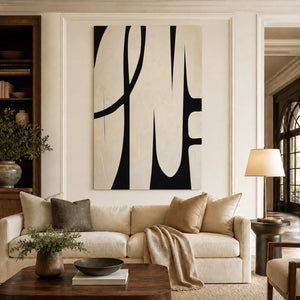 Frameless cream and black curved artwork above a cream sofa beside bookshelves and warm wood.