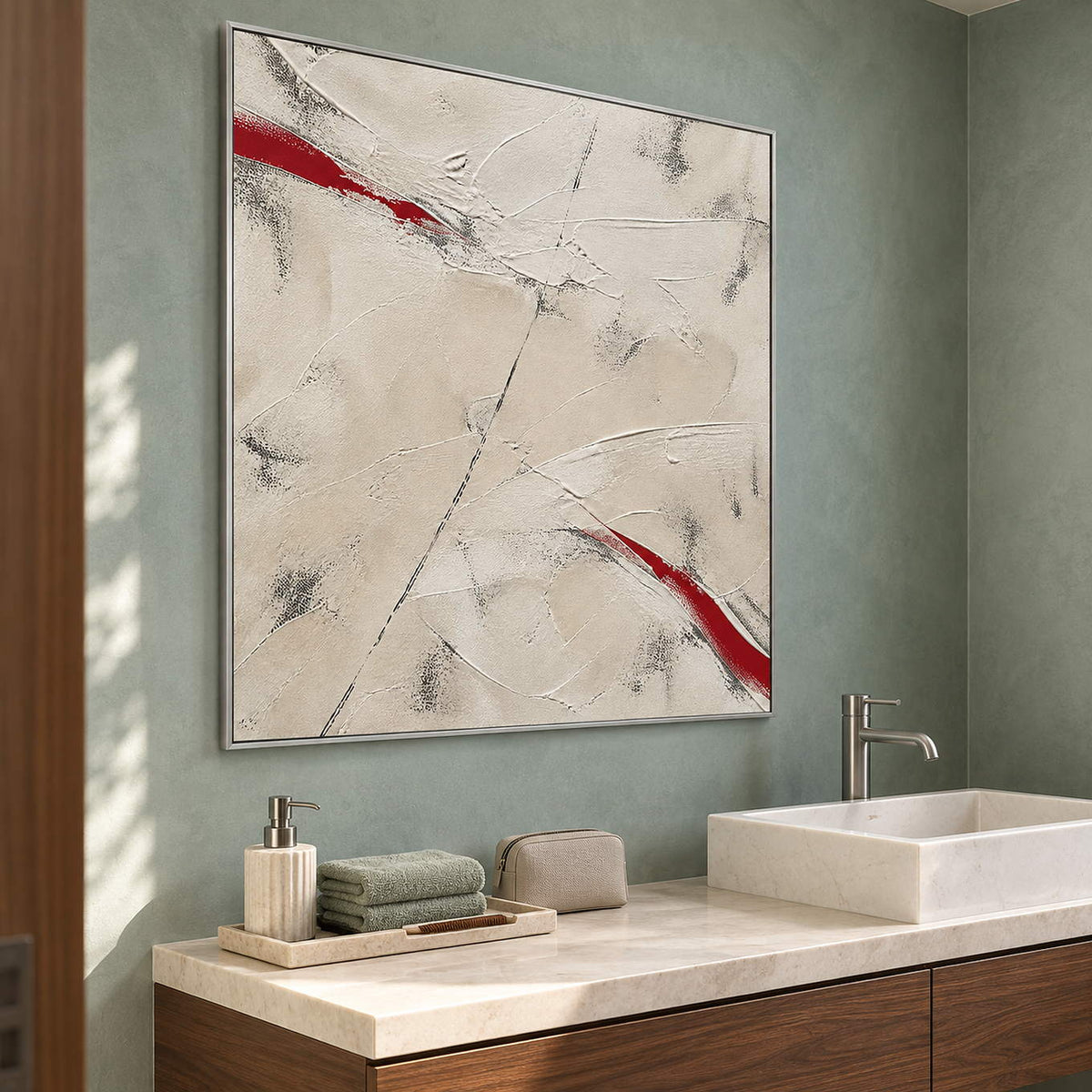Ivory textured abstract painting with red diagonal strokes in a silver frame beside a bathroom vanity.