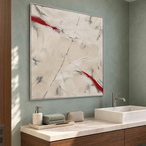 Ivory textured abstract painting with red diagonal strokes in a silver frame beside a bathroom vanity.