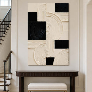 Frameless cream and black artwork above a console beside a staircase.