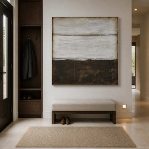Silver-framed horizon-like abstract above an upholstered entry bench beside a dark coat cabinet.