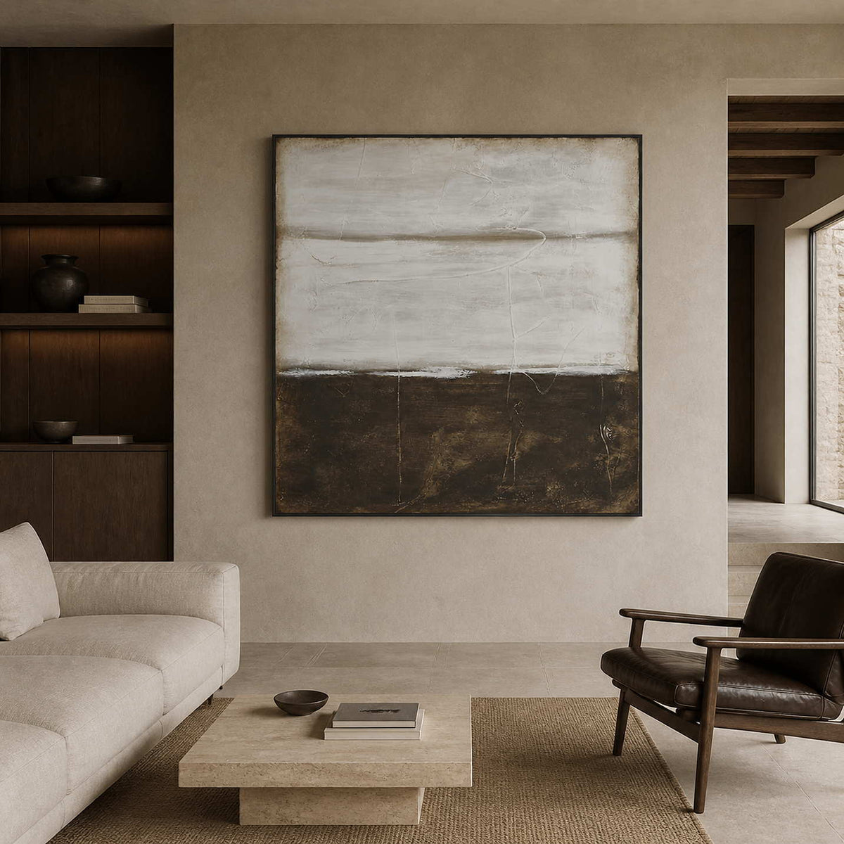 Gray and brown abstract in a black frame between an ivory sofa and leather chair.
