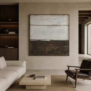 Gray and brown abstract in a black frame between an ivory sofa and leather chair.