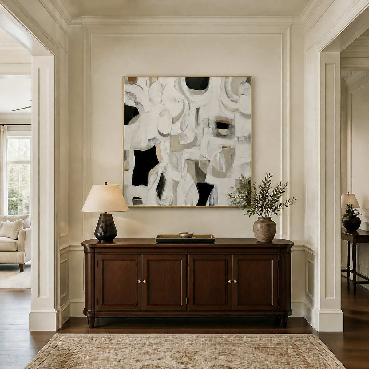 Gold framed square abstract artwork above a dark wood console with decorative branches.