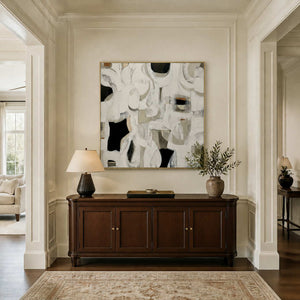 Gold framed square abstract artwork above a dark wood console with decorative branches.