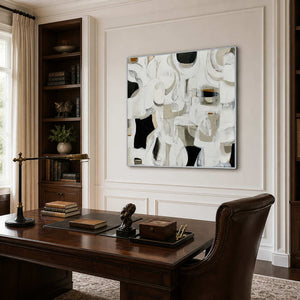 Silver framed abstract artwork behind a wooden desk beside a home office bookcase.