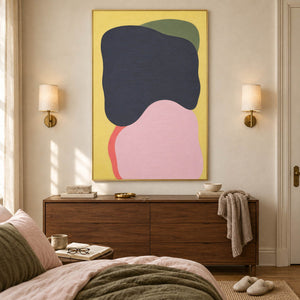 Yellow abstract painting with charcoal, blush, olive, and coral shapes in a gold frame in a bedroom.