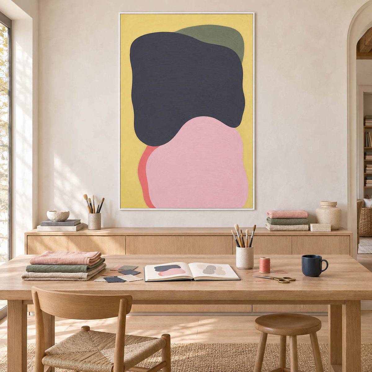 Yellow abstract painting with charcoal, blush, olive, and coral shapes in a white frame in a home craft room.