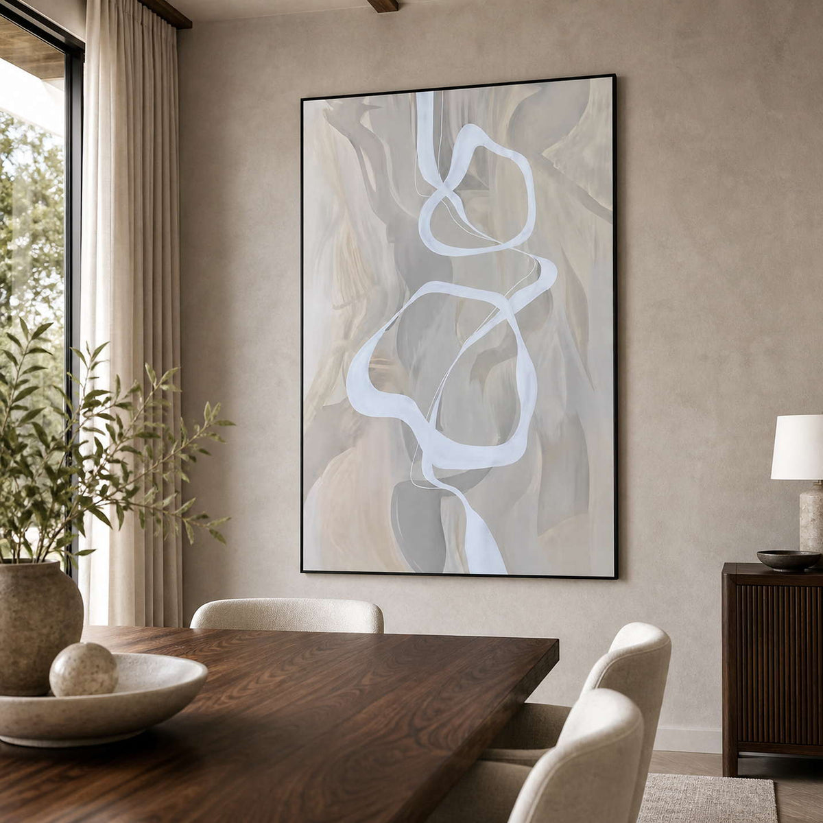 Black framed ribbon abstract artwork beside a wooden dining table and upholstered cream chairs.